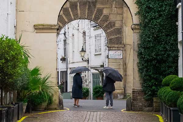 neighbors holding umbrellas under an archway discuss fuel poverty